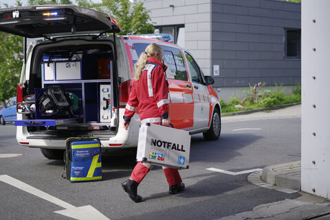 Notärztin trägt Notfallkoffer neben Einsatzfahrzeug her.