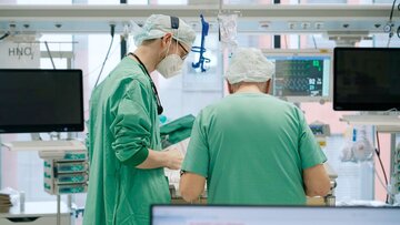 Zwei Männer stehen in OP-Kleidung über einen Patienten gebeugt.