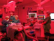 In einem in Rotlicht getauchten OP arbeiten Ärzte am Patienten.